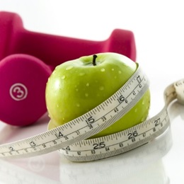 Image of a green apple with a measuring tape wrapped around it and a set of hand weights.